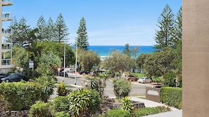 A view of a coastal area with a road, parked cars, and a building with balconies overlooking the ocean.