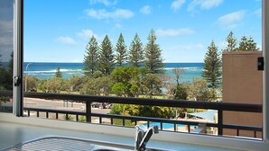 A balcony with a view of the ocean, trees, and a swimming pool.