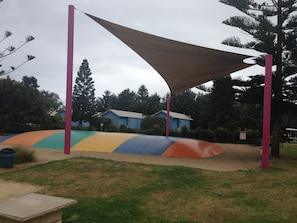 Explore a vibrant playground with a curved play structure and shaded area, set amidst lush greenery and nearby homes.
