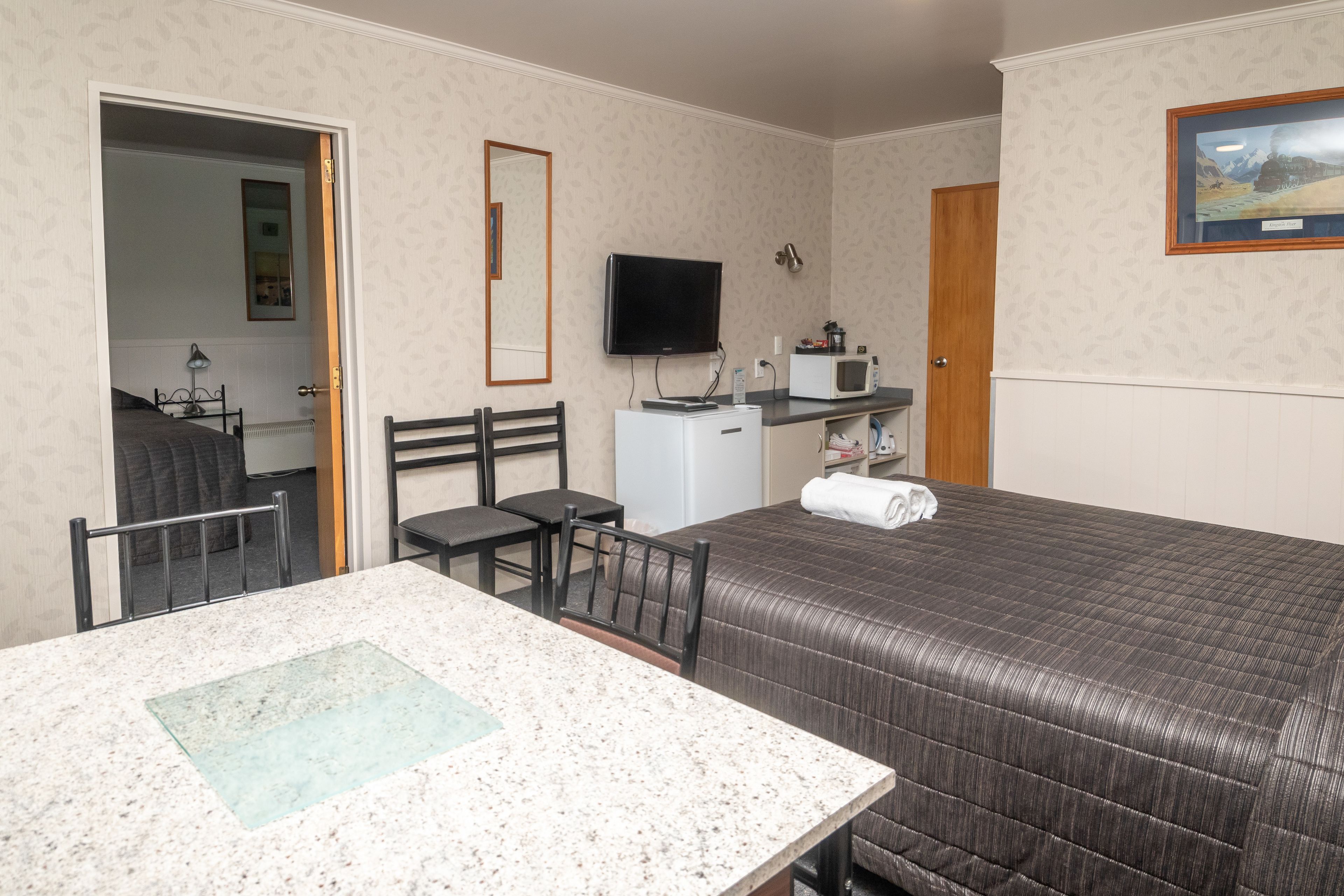 A hotel room with a bed, a desk with a chair, a television, a microwave, and a door leading to another room.