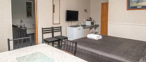 A hotel room with a bed, a desk with a chair, a television, a microwave, and a door leading to another room.