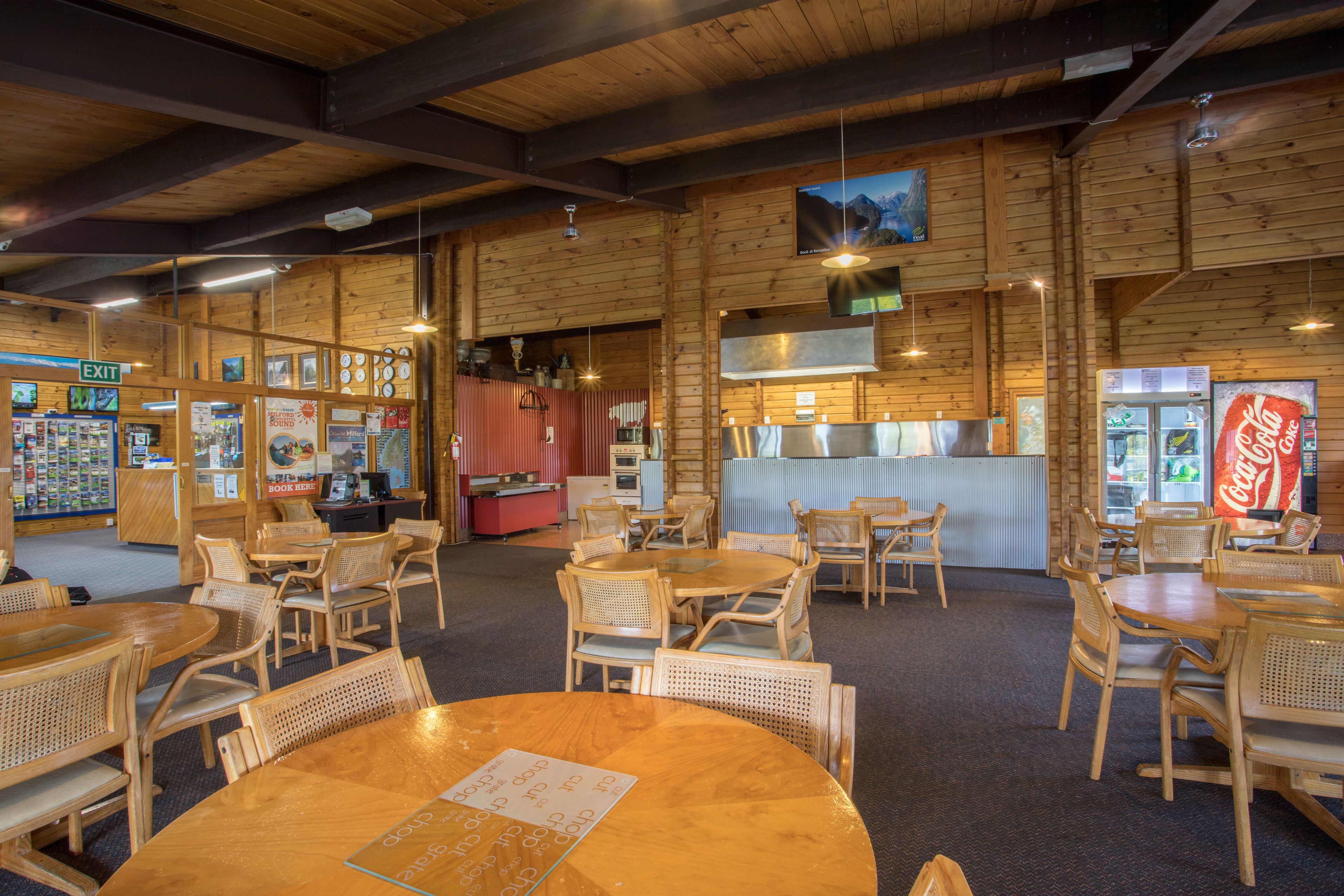A restaurant with wooden interiors, tables, chairs, a Coca-Cola refrigerator, and a menu on the tables.