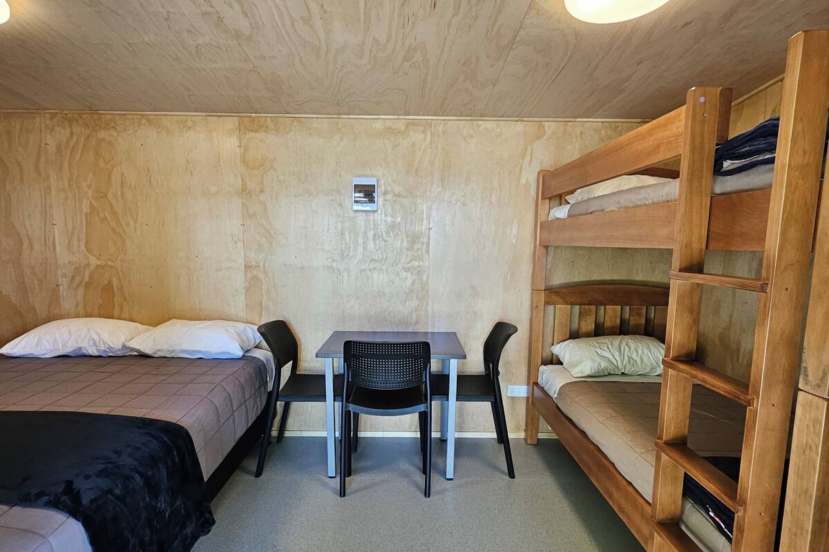Ein Zimmer mit zwei Einzelbetten, einem kleinen Tisch mit Stühlen und einem Etagenbett.