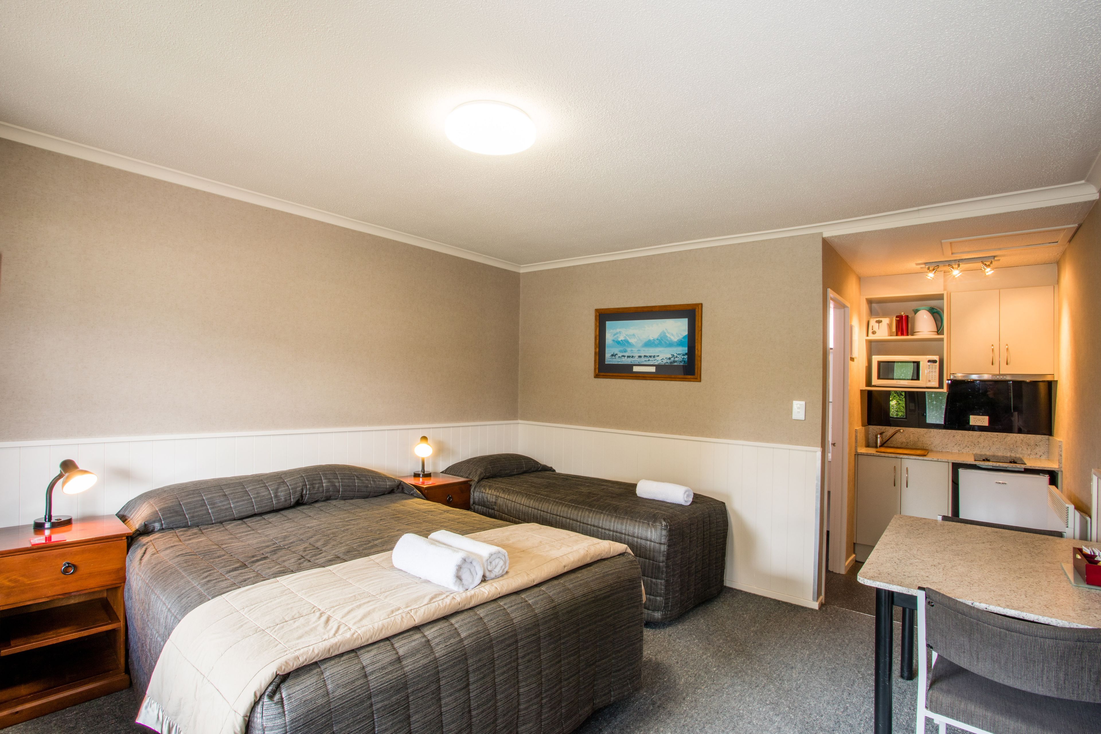 Habitación de hotel con dos camas, una kitchenette pequeña y un cuadro en la pared.