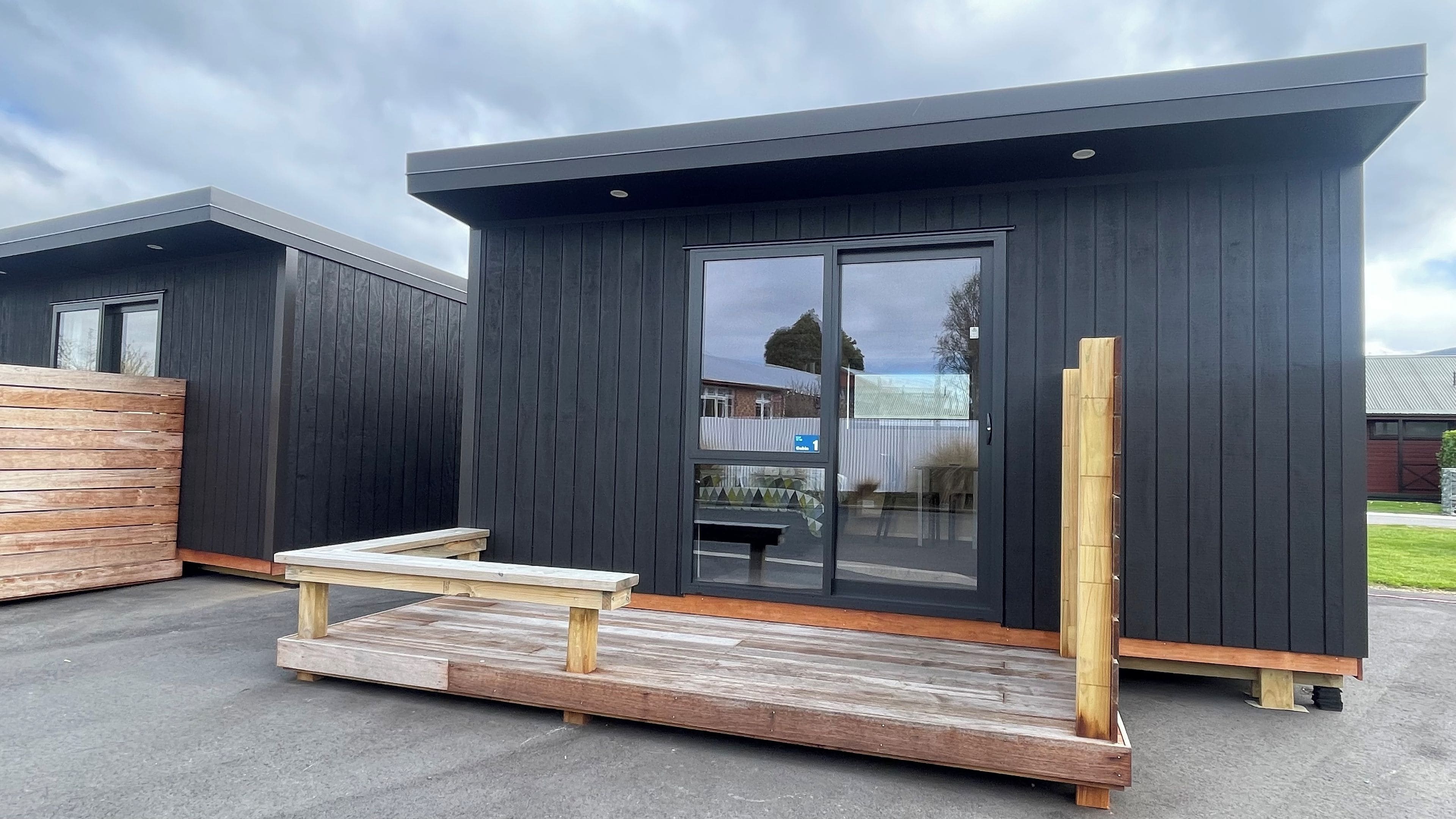 A modern, dark-colored building with a wooden bench and a small table outside.