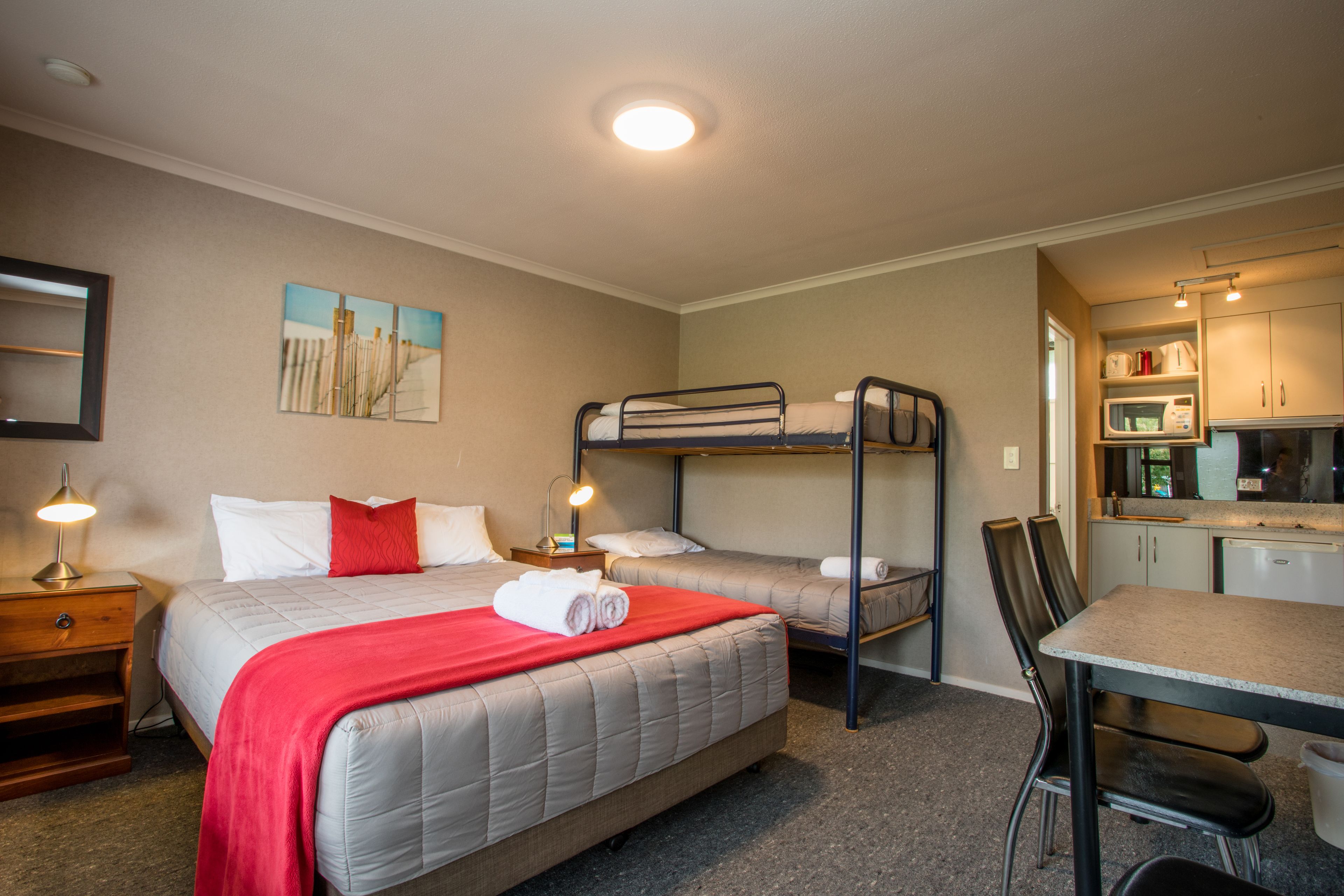 A hotel room with a bunk bed, a desk, and a kitchenette.