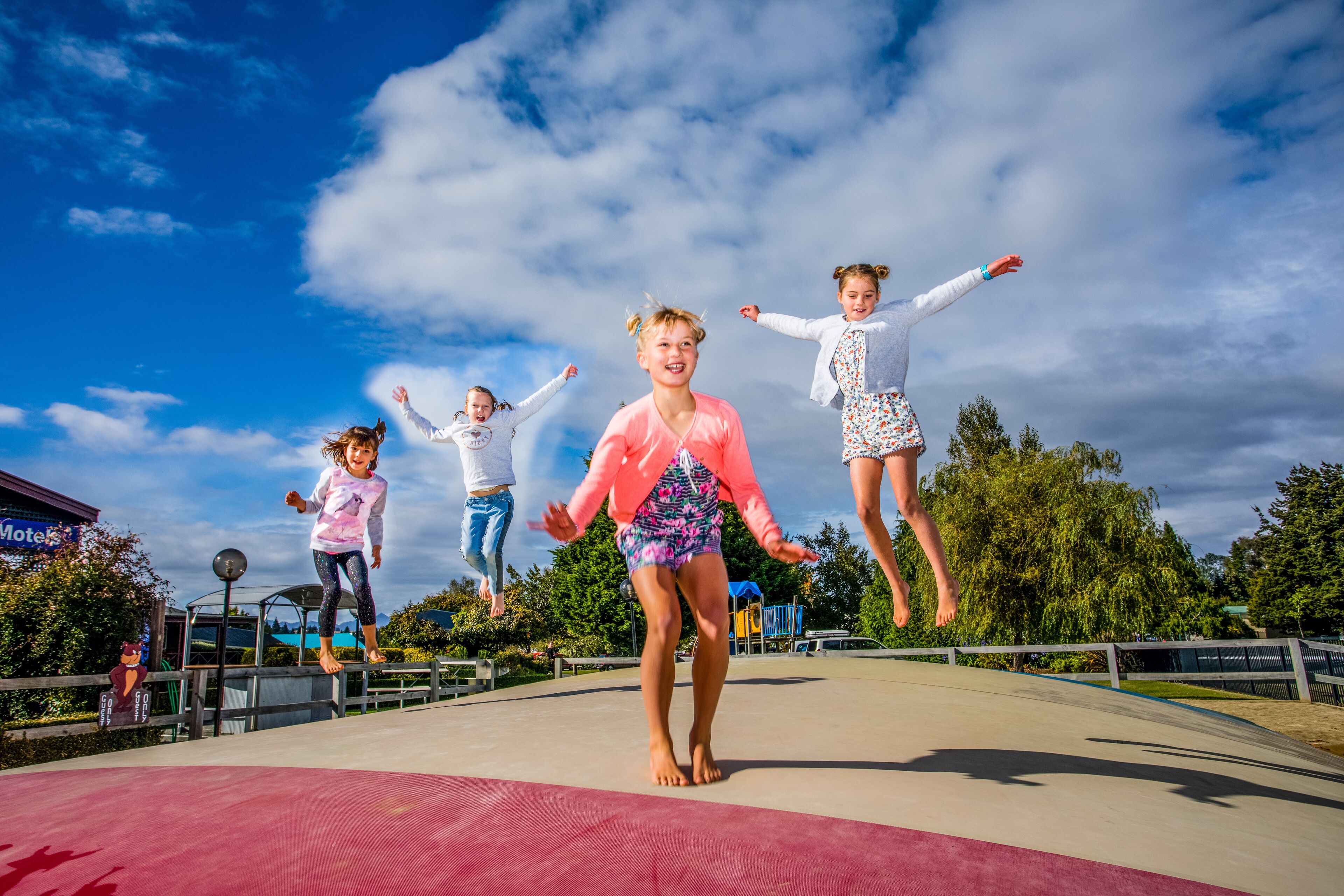 A group of children jumping on a trampoline in an outdoor setting with a clear sky.