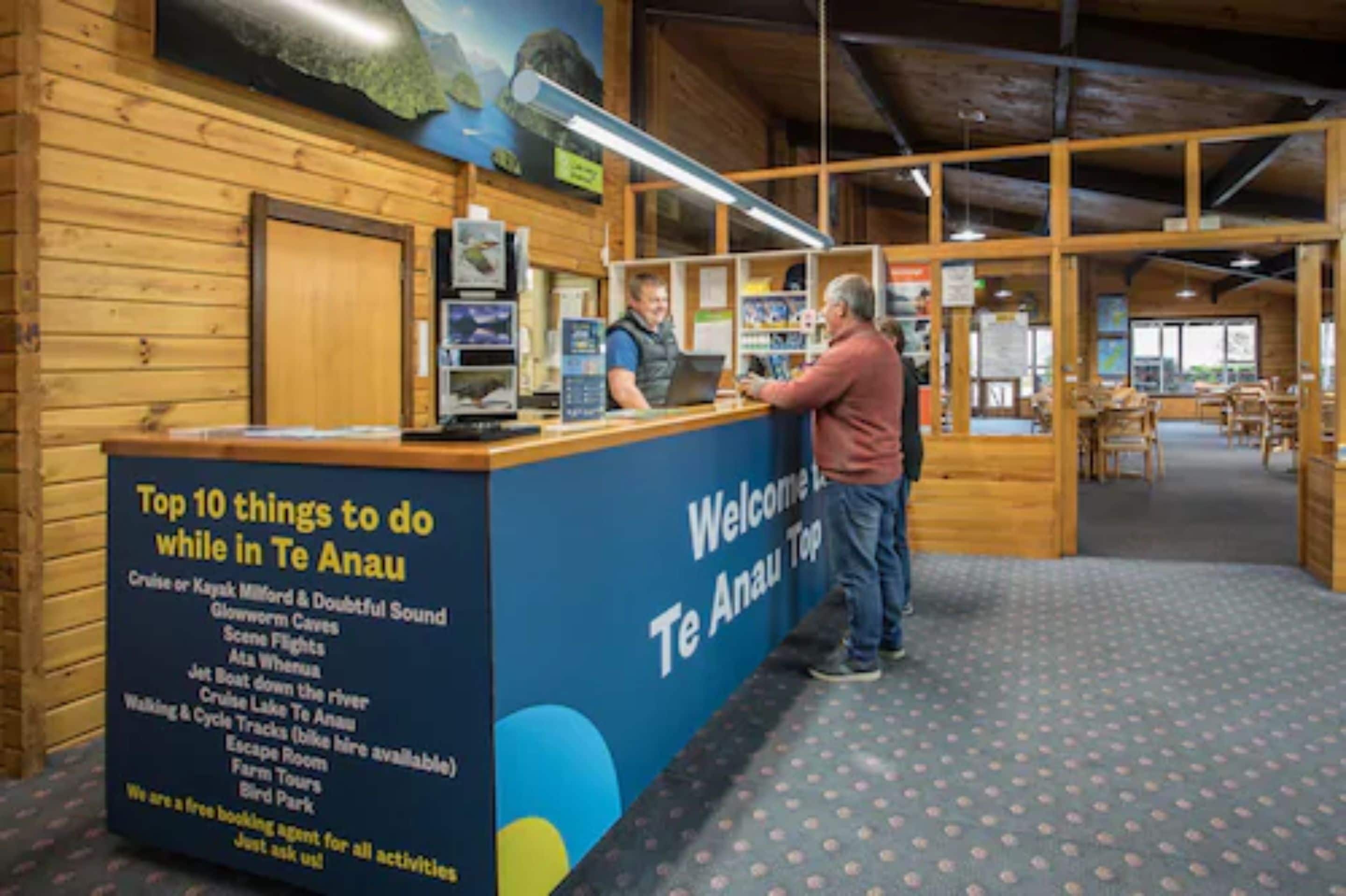 A reception desk with a sign listing top activities in Te Anau, including a free booking agent.