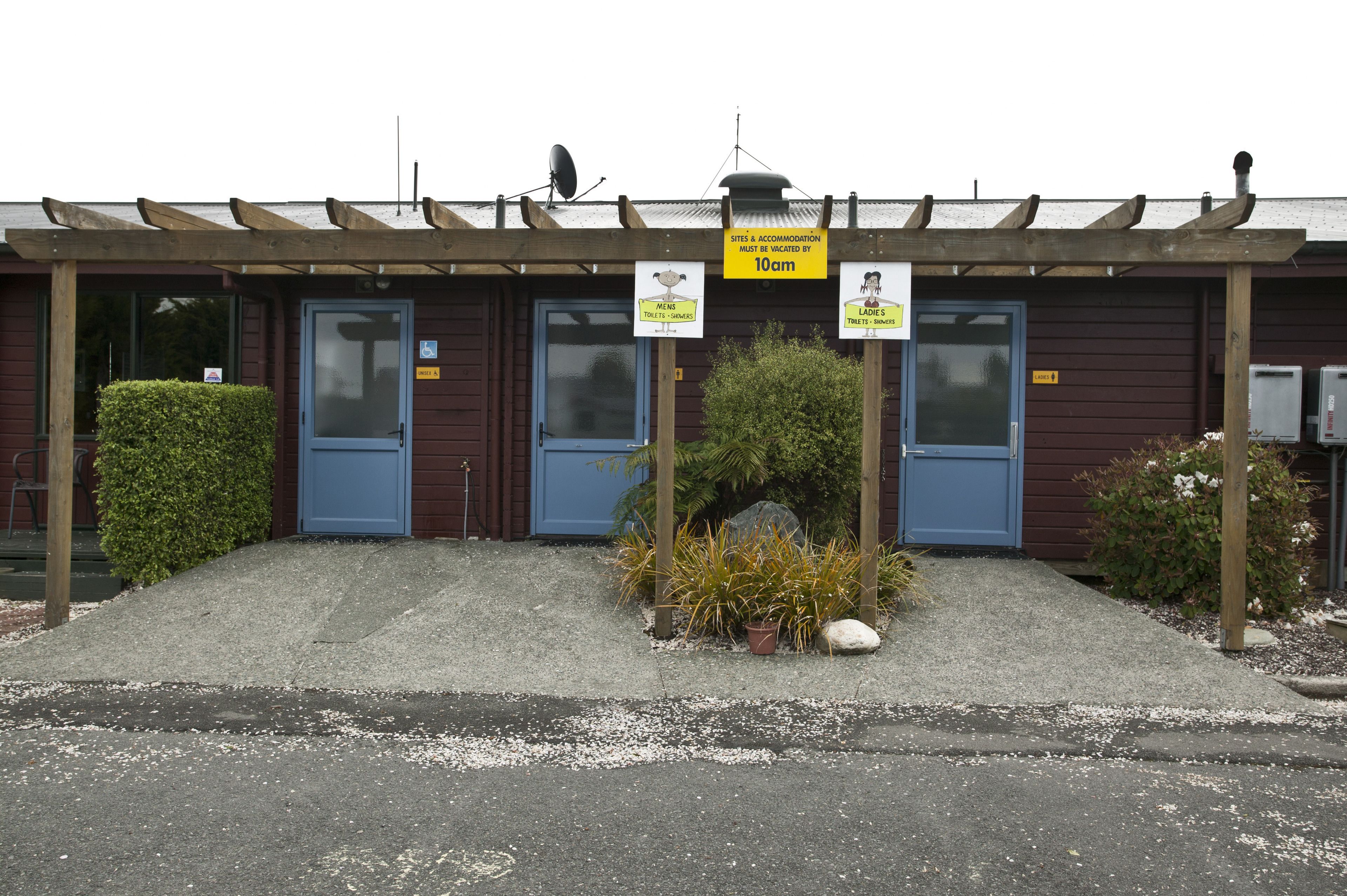 A building with two blue doors, a covered outdoor area, and signs indicating amenities like toilets and a ladies' room.