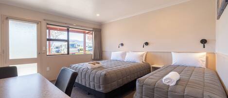 A hotel room with two beds, a table, and a window with a view of the outside.