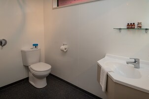 Un baño con inodoro, lavamanos y estante con artículos de aseo.