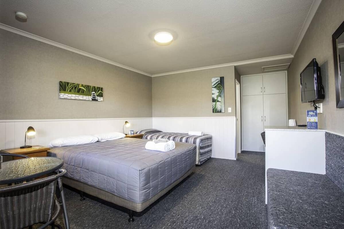 Ein Hotelzimmer mit einem Bett, zwei Nachttischen, einem Schreibtisch, einem Sessel und einem Fernseher.