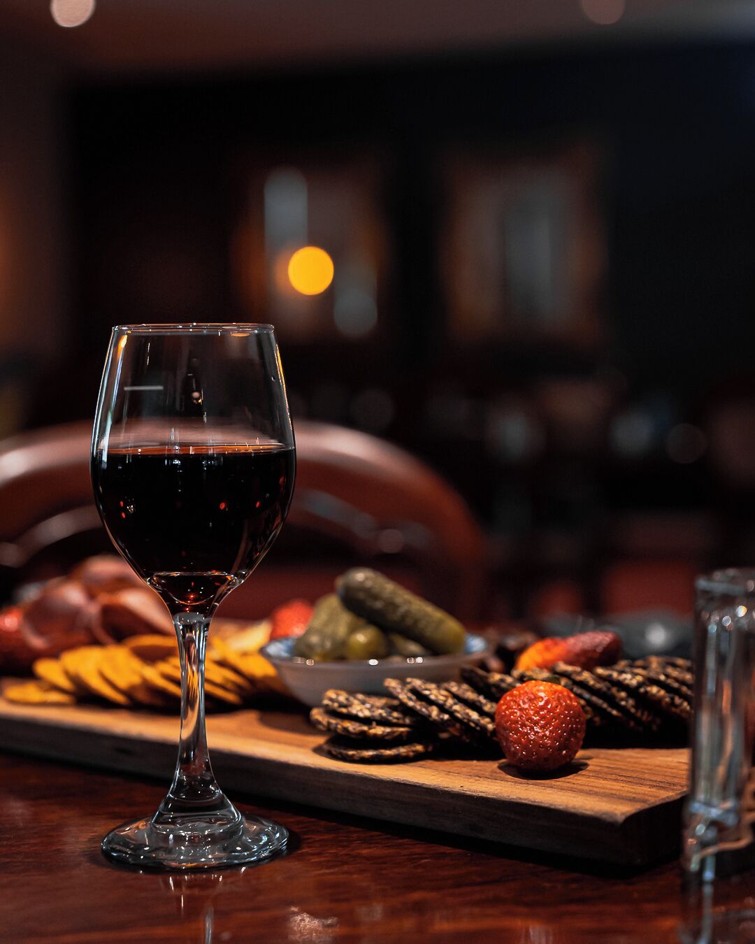 A wine glass filled with red wine on a wooden table, surrounded by various snacks and pickles.