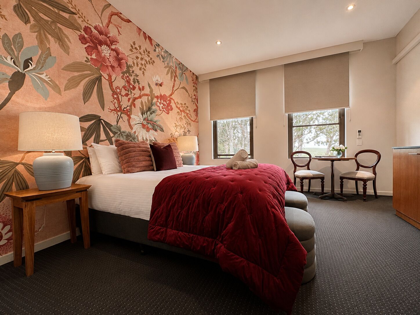 A hotel room with a bed, two bedside tables, a desk, two chairs, and a window.