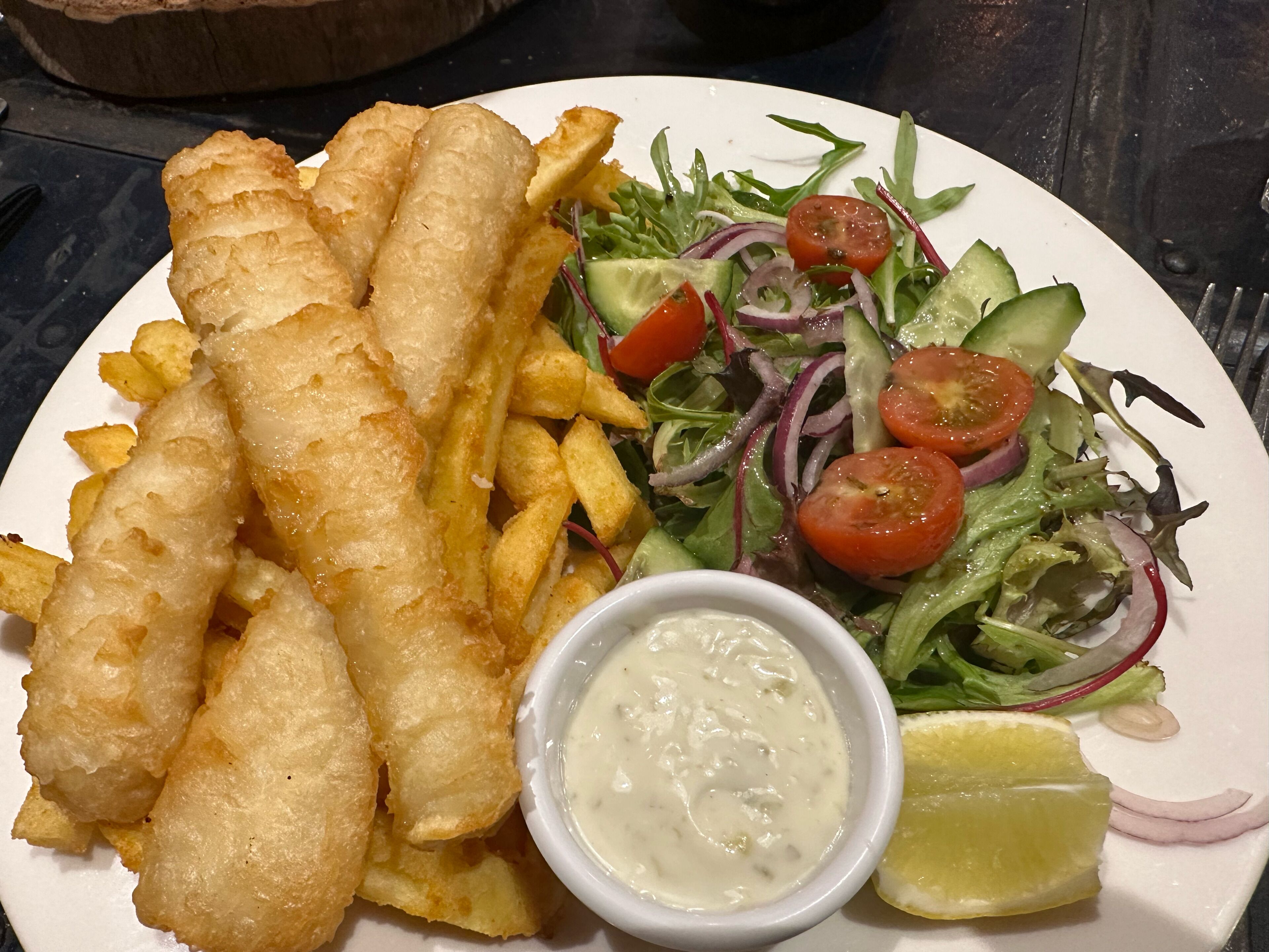 Une assiette de poisson-frites, une salade et un petit bol de sauce.