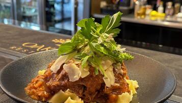 A dish with shredded meat, pasta, and garnishes on a black plate.