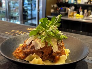 A dish with shredded meat, pasta, and garnishes on a black plate. - The Grand Oaks Resort (Beechworth)