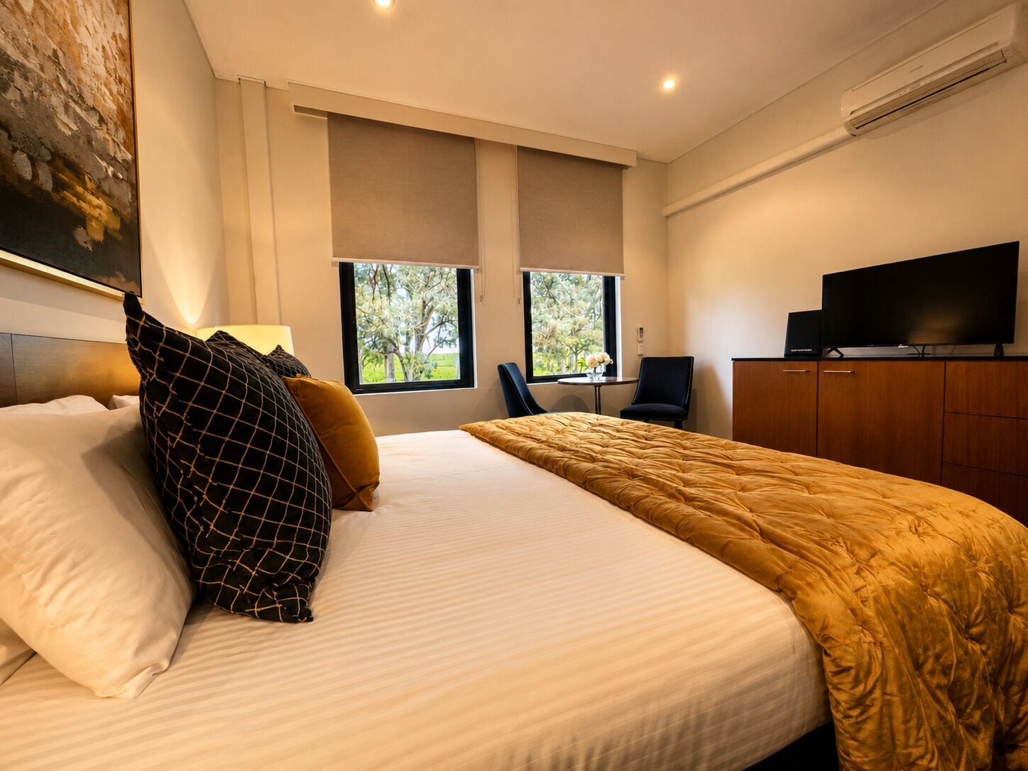 A modern hotel room with a large bed, two windows, a flat-screen TV, and a desk.