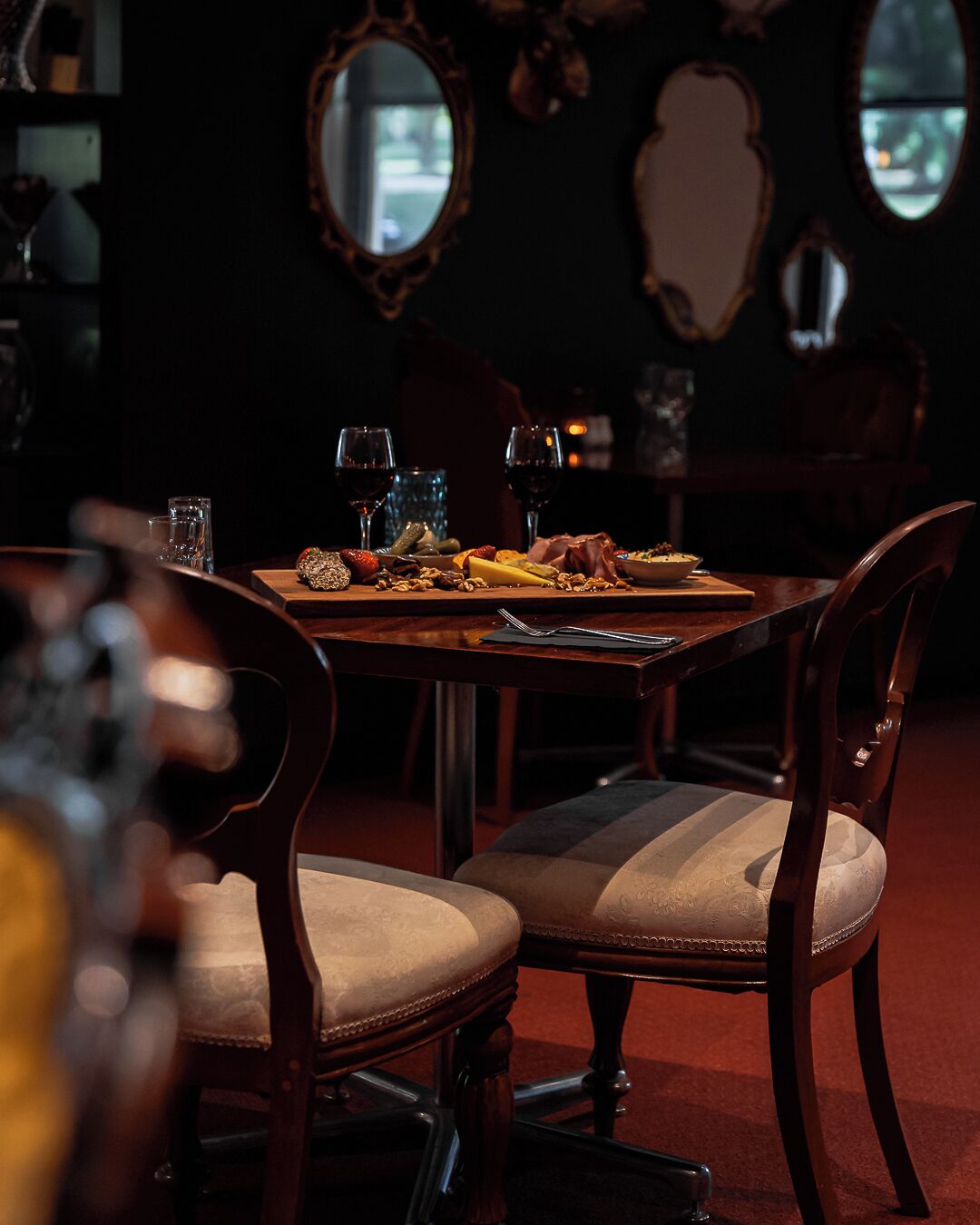 Un coin repas avec une table en bois dressée pour deux personnes, agrémentée d’un plateau de fromages, de verres à vin et d’un petit bol de noix.
