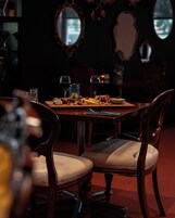 Uma sala de jantar com uma mesa de madeira posta para dois, com um prato de queijos, copos de vinho e uma pequena tigela de nozes.