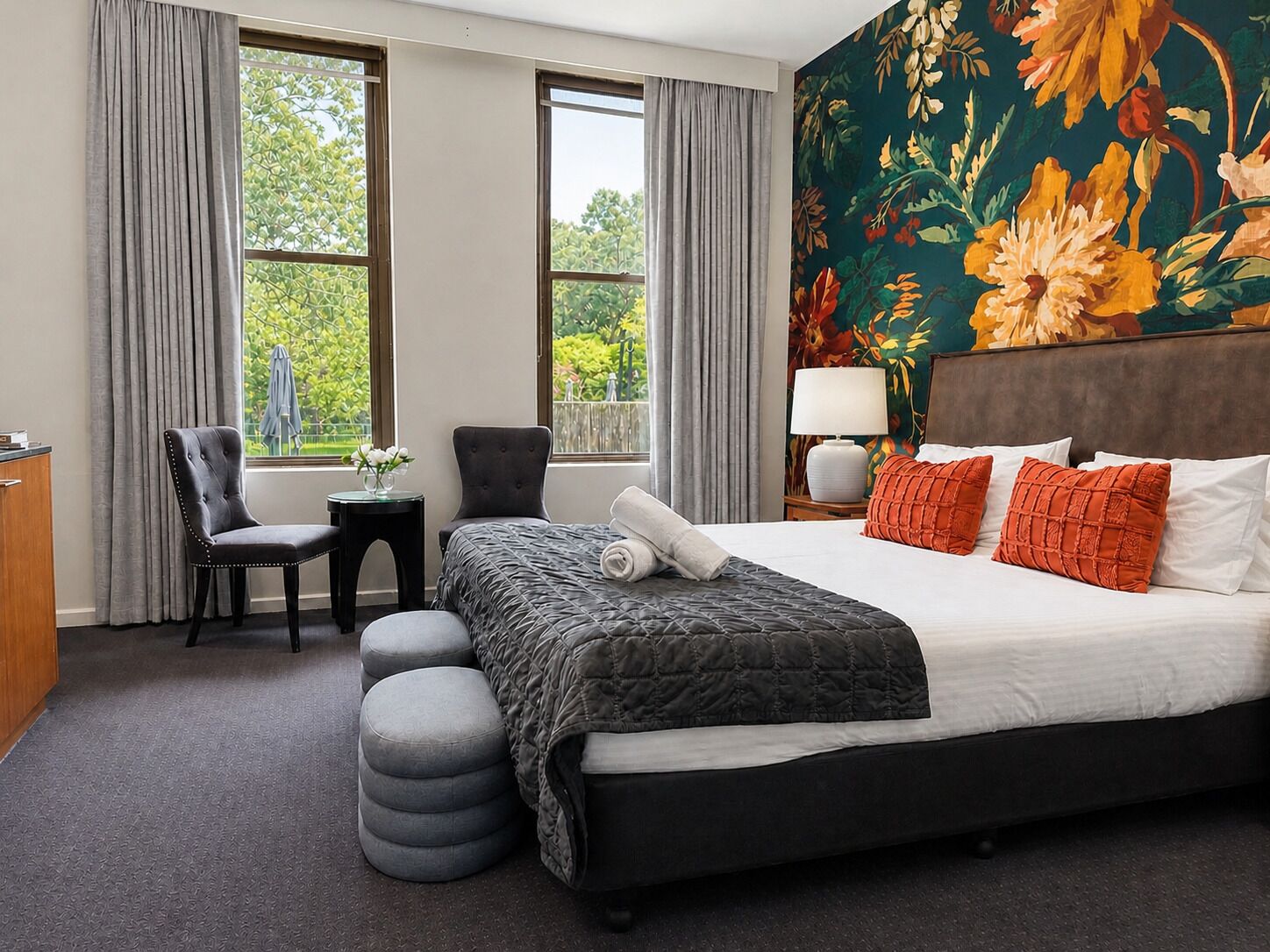 A hotel room with a bed, two chairs, a small table, and a view of greenery outside.