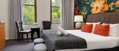 A hotel room with a bed, two chairs, a small table, and a view of greenery outside.
