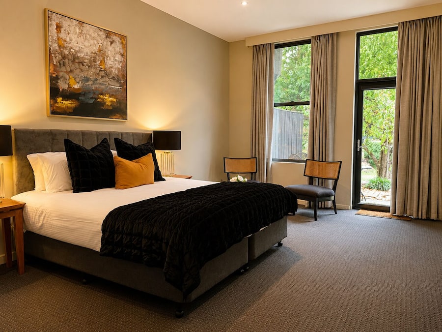 A bedroom with a large bed, two bedside tables, a chair, and a window with curtains.