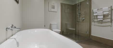 Een moderne badkamer met een groot, wit bad, een douche met glazen wanden en een toilet.
