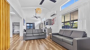 A modern living room with a grey sofa, a dining area, and a kitchen. - Cairns Coconut Holiday Resort (Woree)