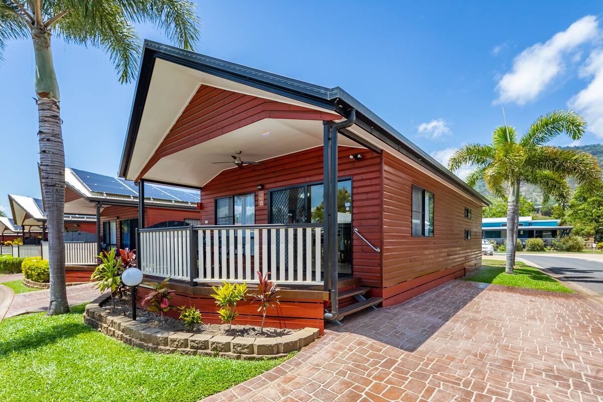 Una casa de madera roja con balcón, paneles solares y entrada pavimentada.