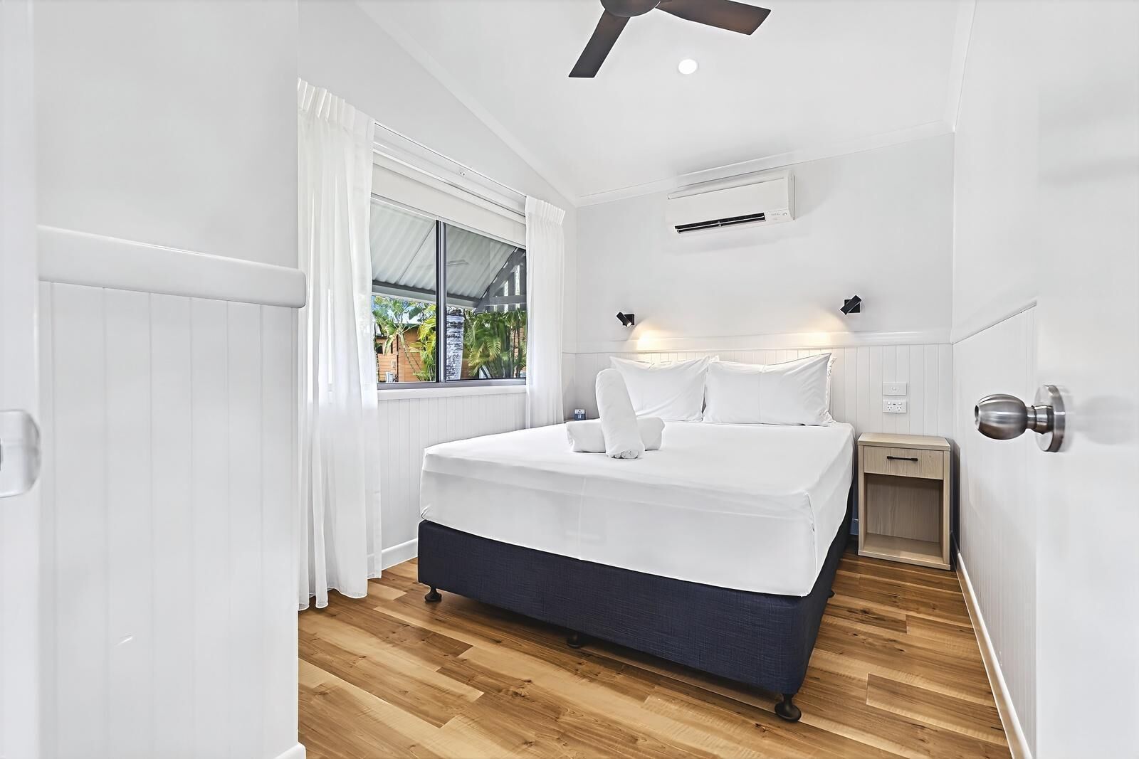 Un dormitorio moderno con una cama grande, paredes blancas, suelo de madera y un ventilador de techo.
