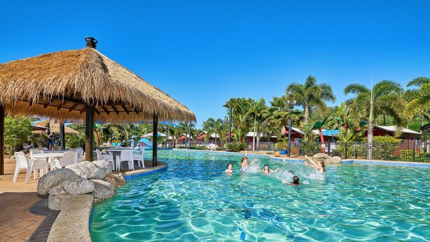 A clear blue pool with a thatched roof structure, surrounded by palm trees and lounge chairs. - Cairns Coconut Holiday Resort (Woree)