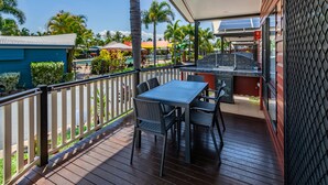 A covered outdoor area with a table and chairs, a grill, and a view of a pool and palm trees. - Cairns Coconut Holiday Resort (Woree)