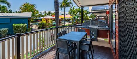 A covered outdoor area with a table and chairs, a grill, and a view of a pool and palm trees.