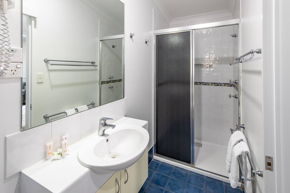 Un baño con lavamanos blanco, espejo y ducha con puerta de cristal.