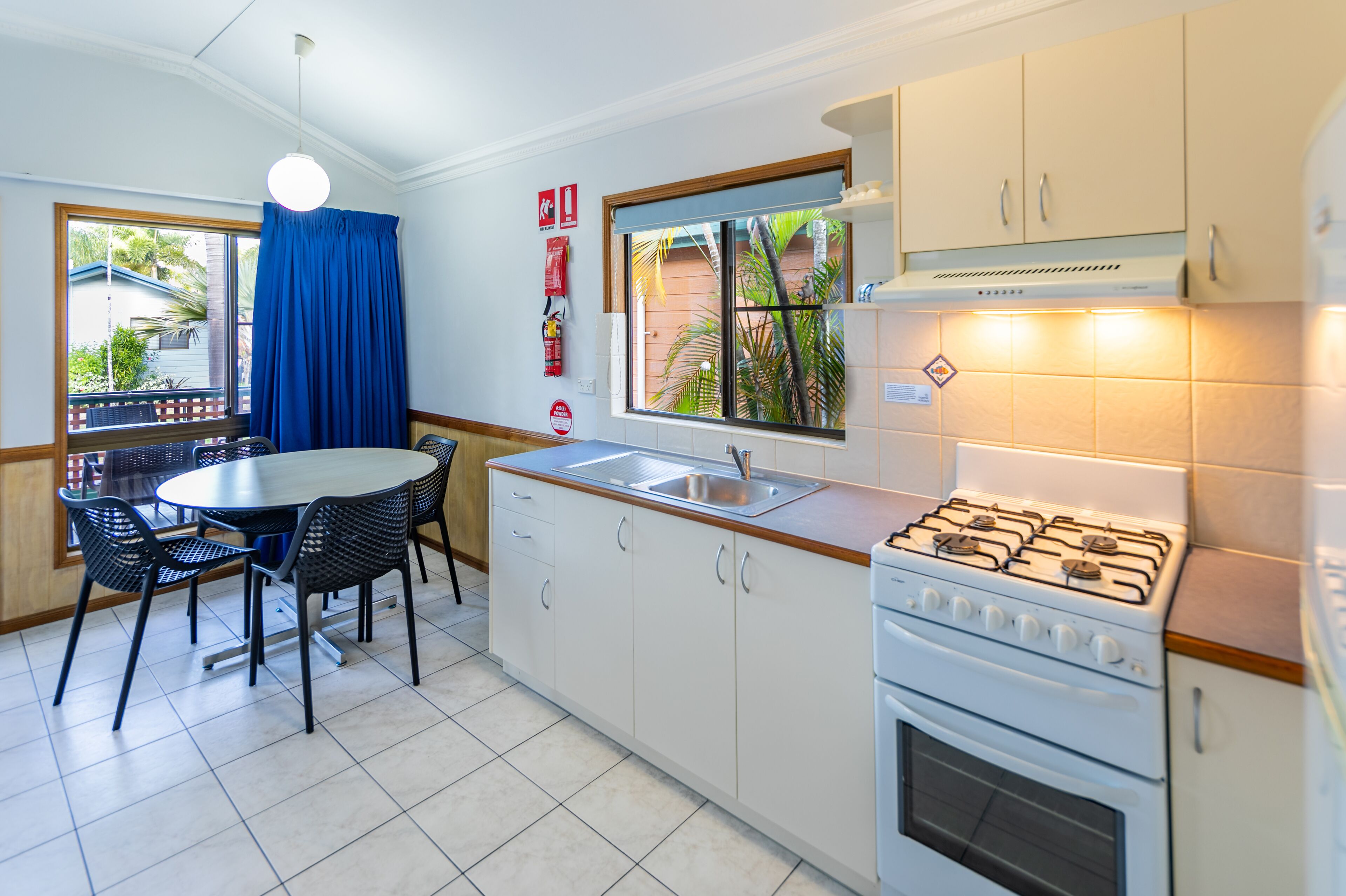 Una cocina compacta con estufa a gas, un lavamanos y una zona de comedor con sillas y mesa.