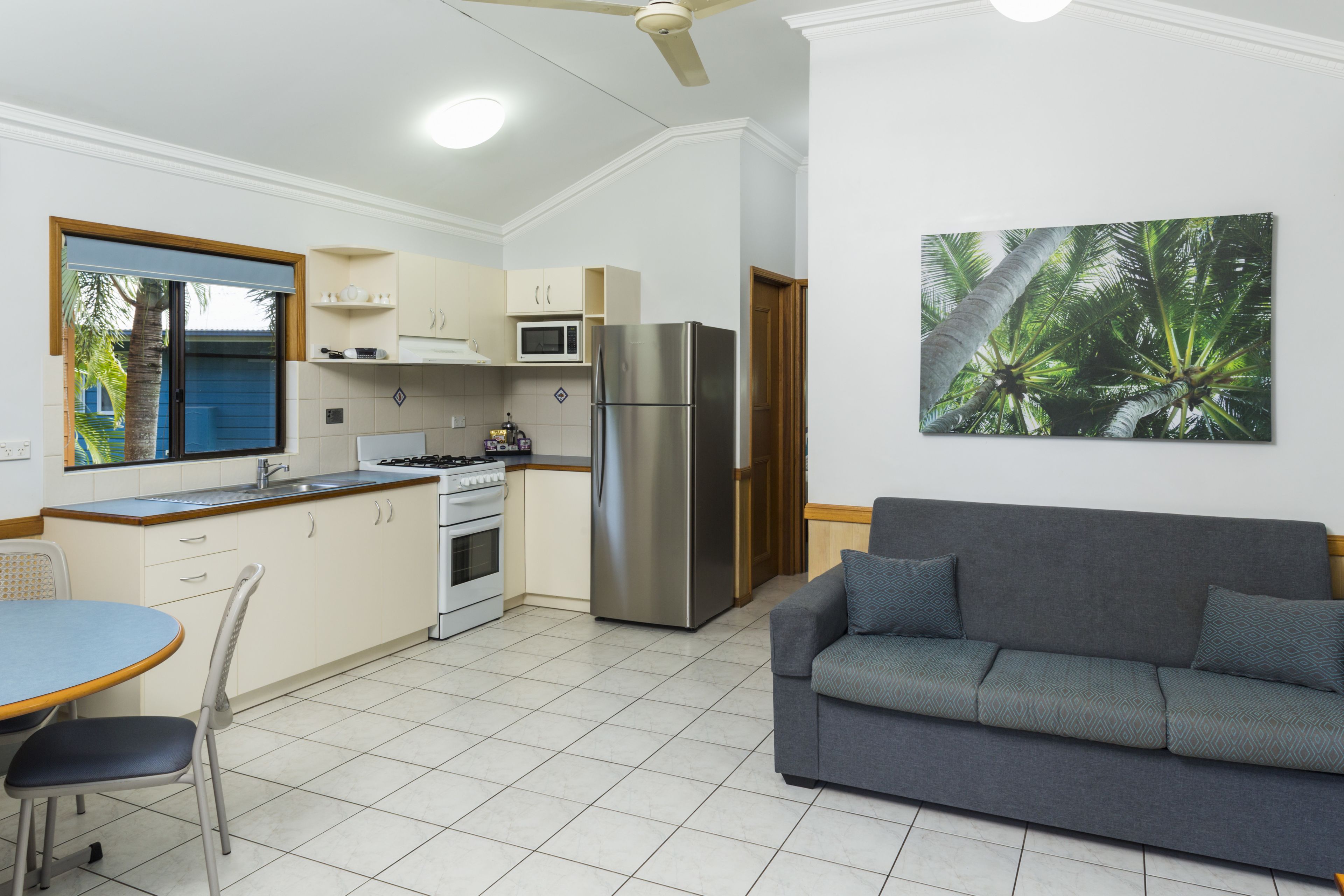 A modern kitchen with a refrigerator, microwave, and stove. There is a dining area with a table and chairs, and a gray sofa in the living room.