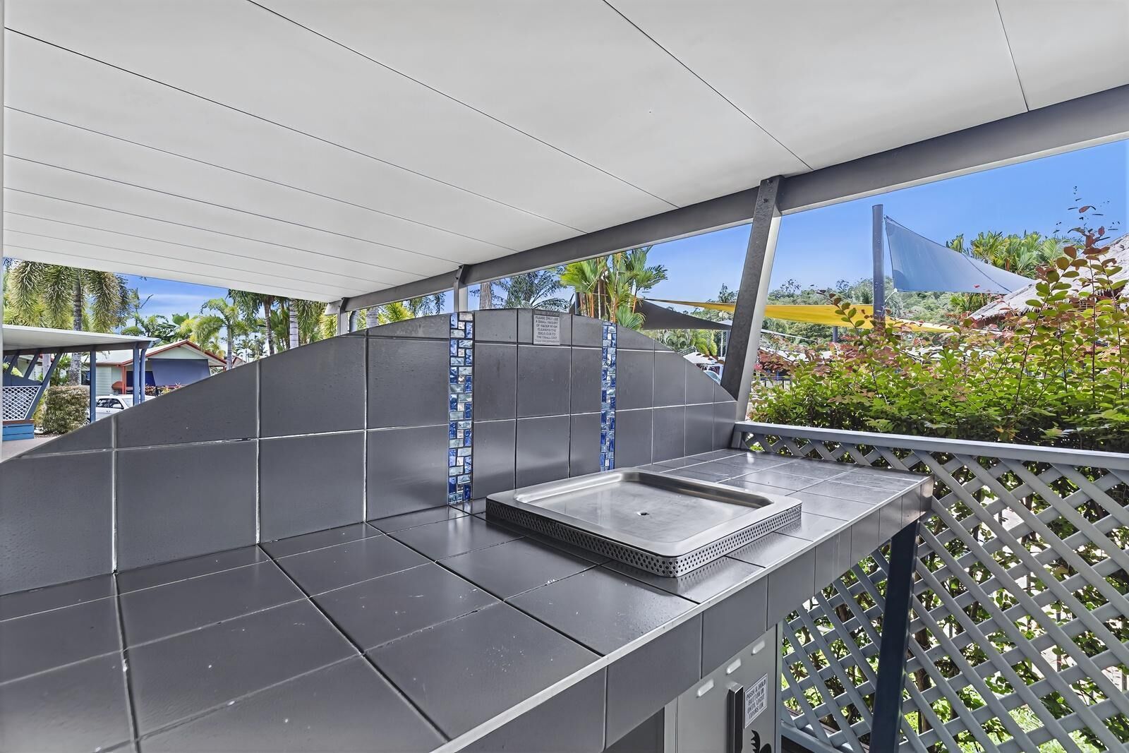 An outdoor kitchen area with a metal sink and a tiled backsplash.