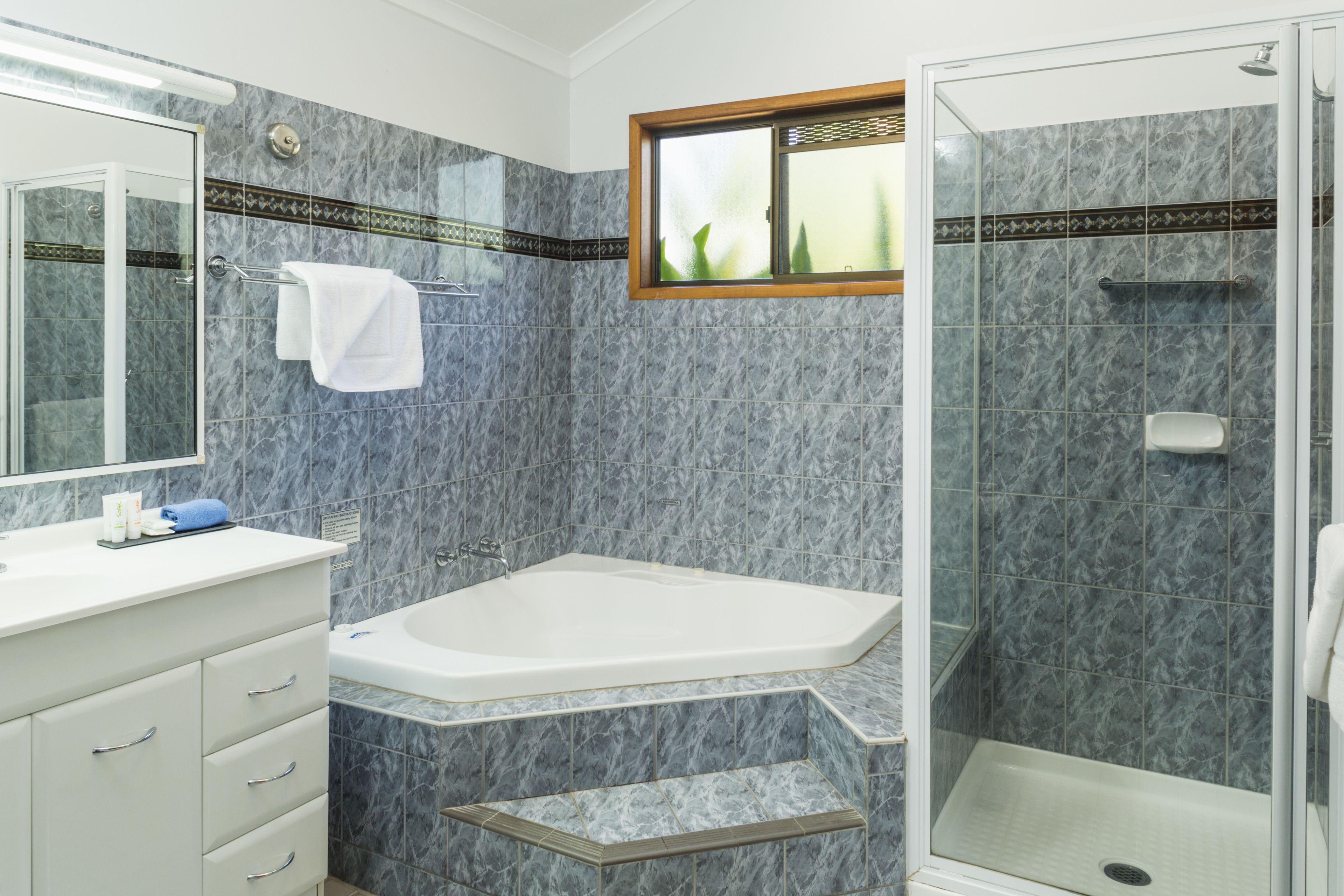 Un baño con pared de mármol, bañera, ducha y tocador con cajones.