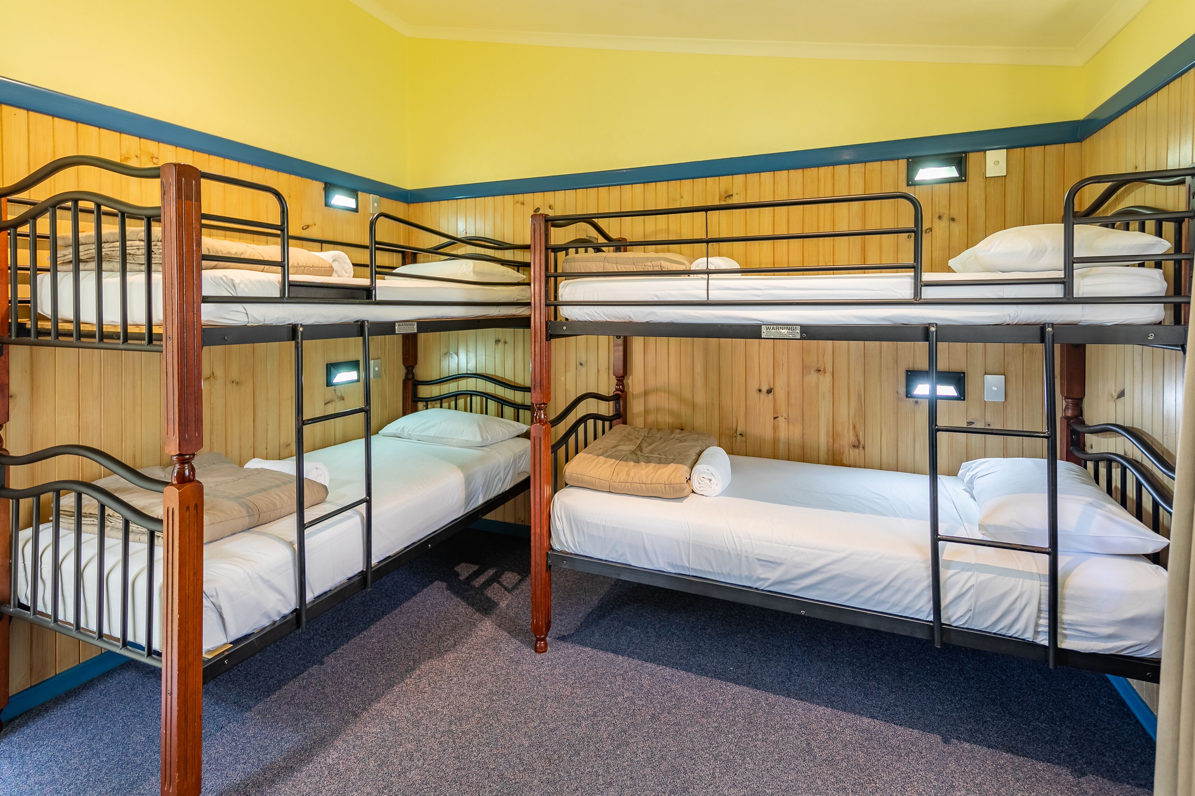 A bunk room with three beds, wooden panel walls, and carpeted floor.