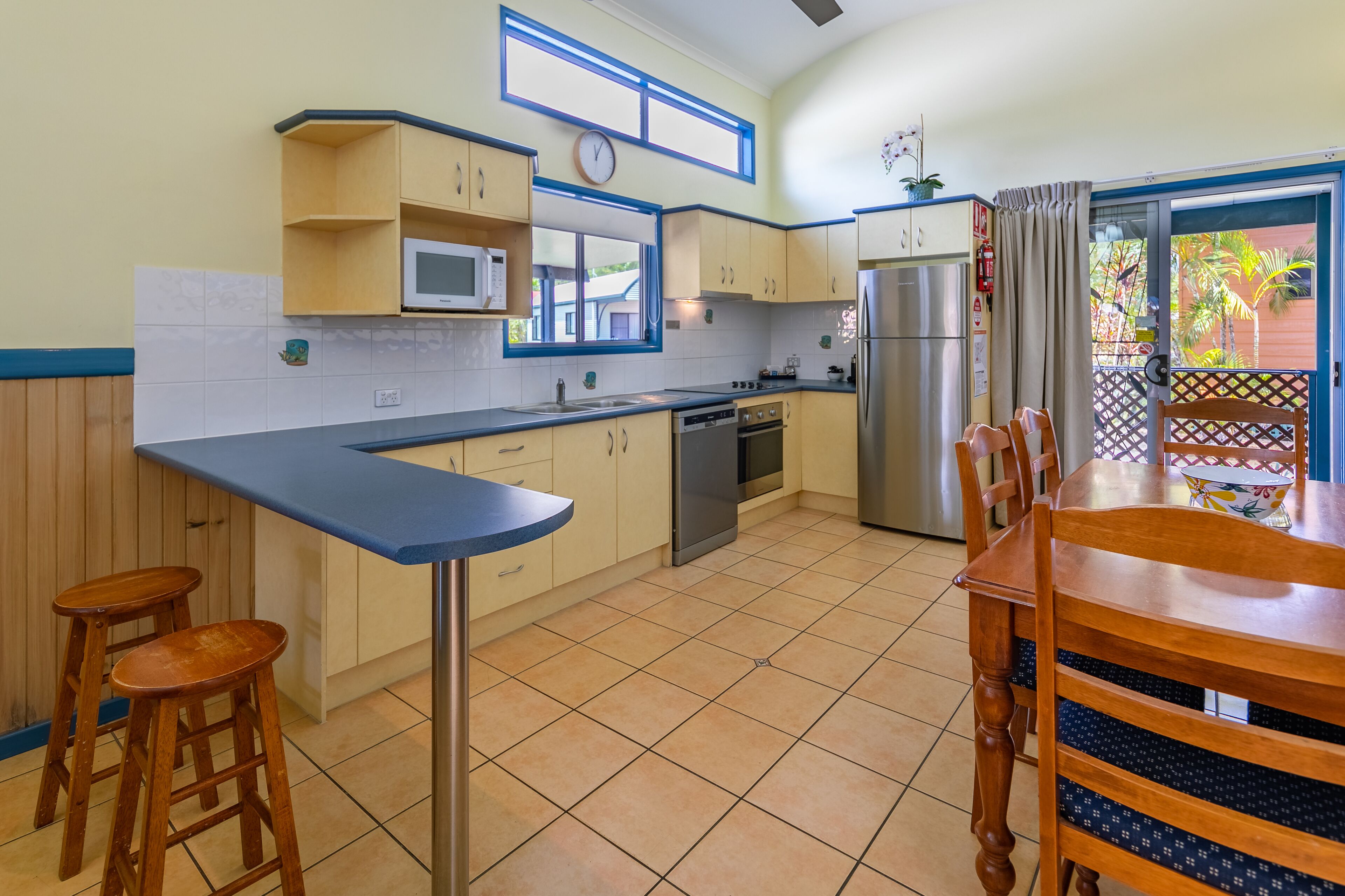 A compact kitchen with a microwave, stove, and refrigerator. There are wooden stools and a dining table with chairs.