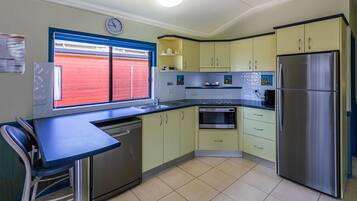 A kitchen with a stainless steel refrigerator, a microwave, and a dishwasher. There is a window with red shutters and a clock on the wall.