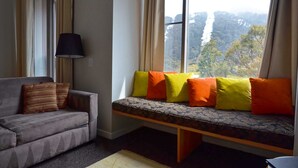 A room with a sofa and a window seat with cushions. - Squatter's Run Apartments (Thredbo)