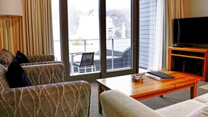 A living room with a sofa, armchair, and a television on a wooden stand. - Squatter's Run Apartments (Thredbo)