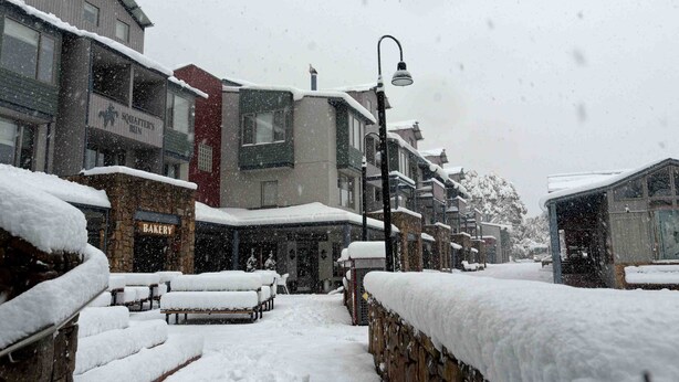 A snow-covered street with buildings, including a bakery and a bar. - Squatter's Run Apartments (Thredbo)