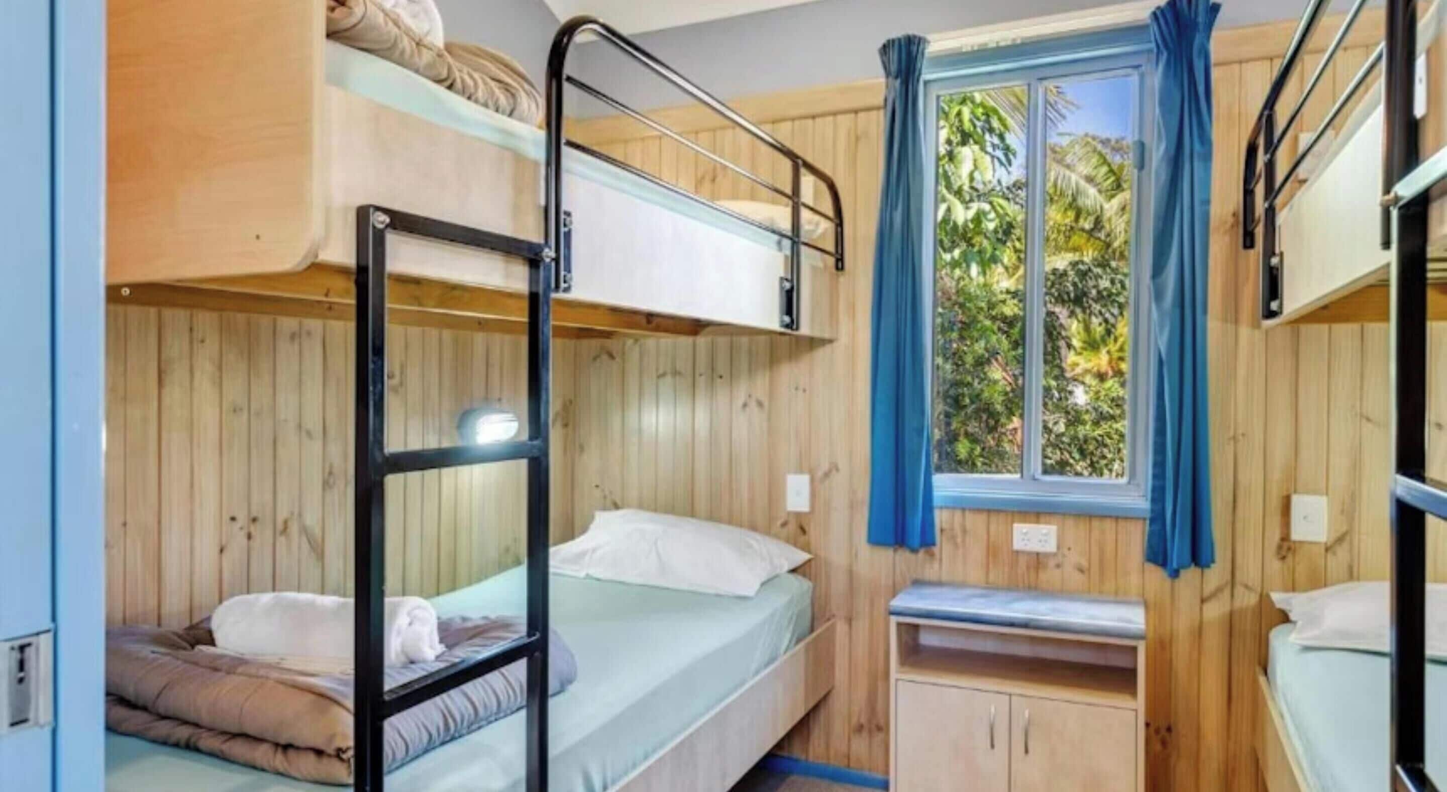 Dormitorio con literas, ventana, paredes de madera y un mueble pequeño.