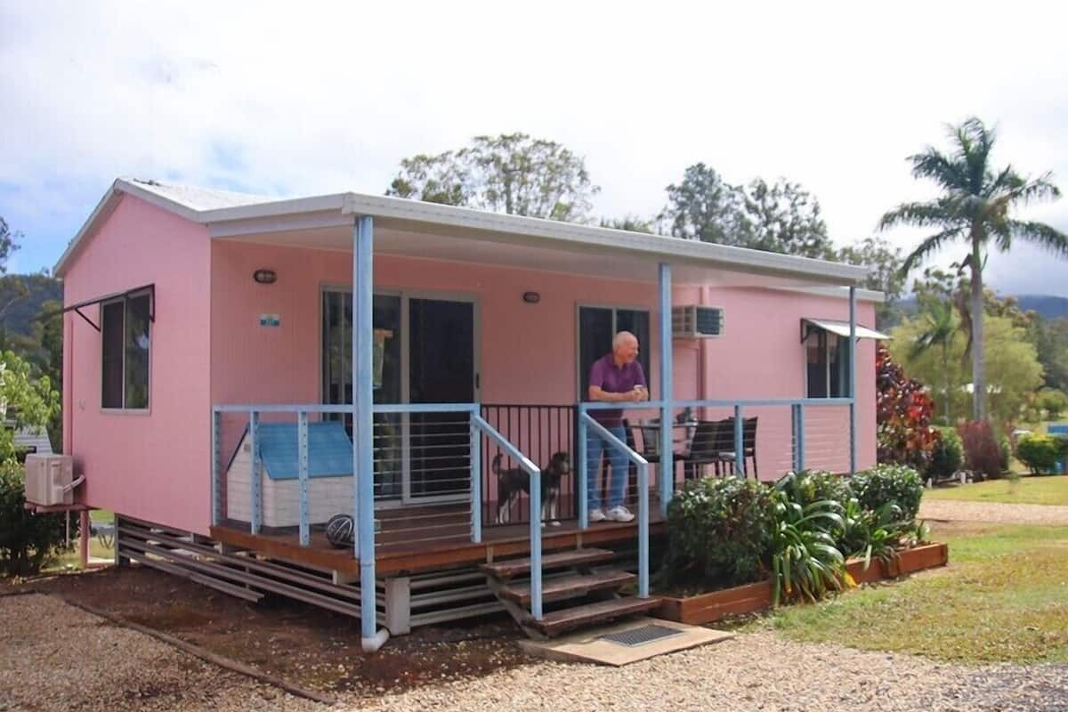 A pink single-story house with a porch, a small staircase, and a dog on the porch.