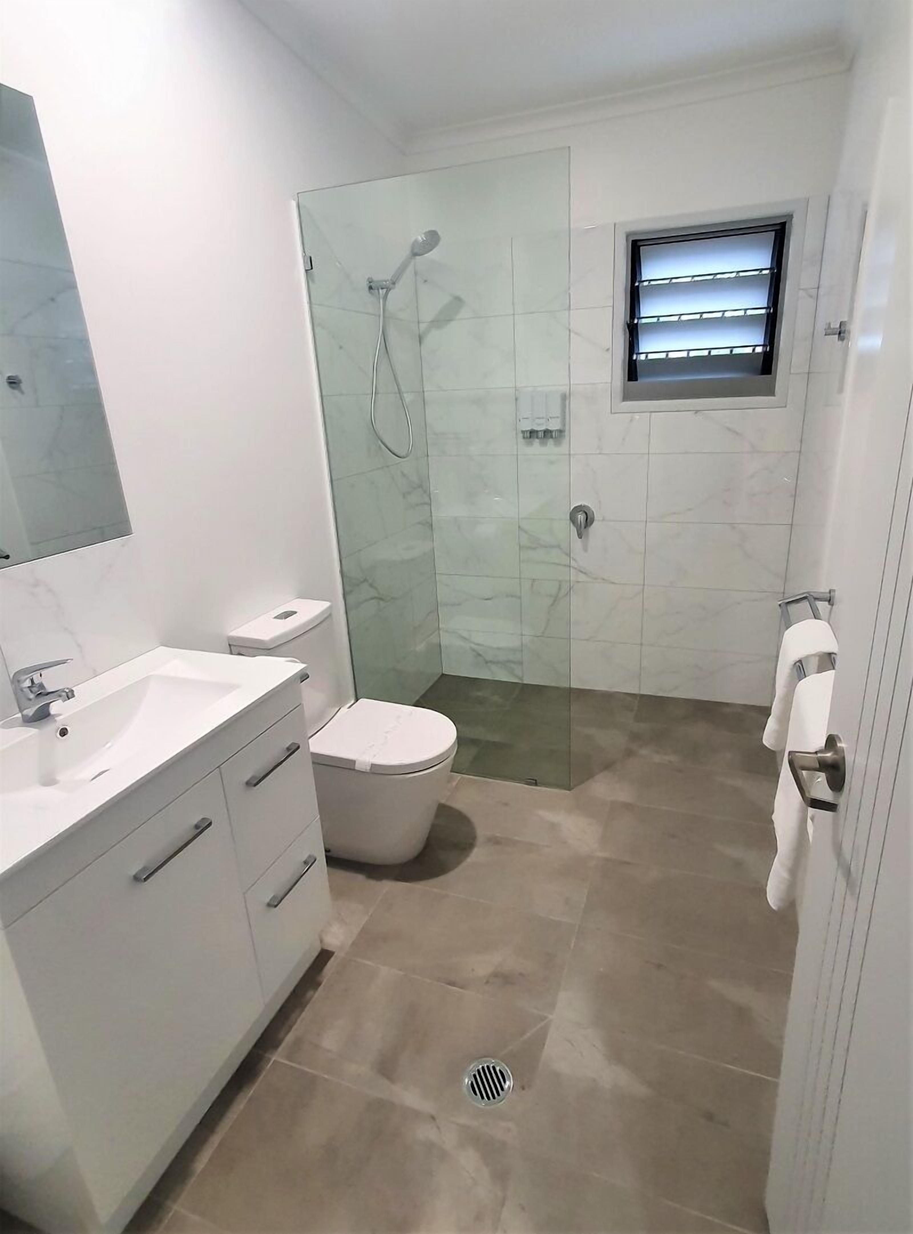Un baño moderno con cabina de ducha de vidrio, inodoro, lavamanos con espejo y perchero para toallas.