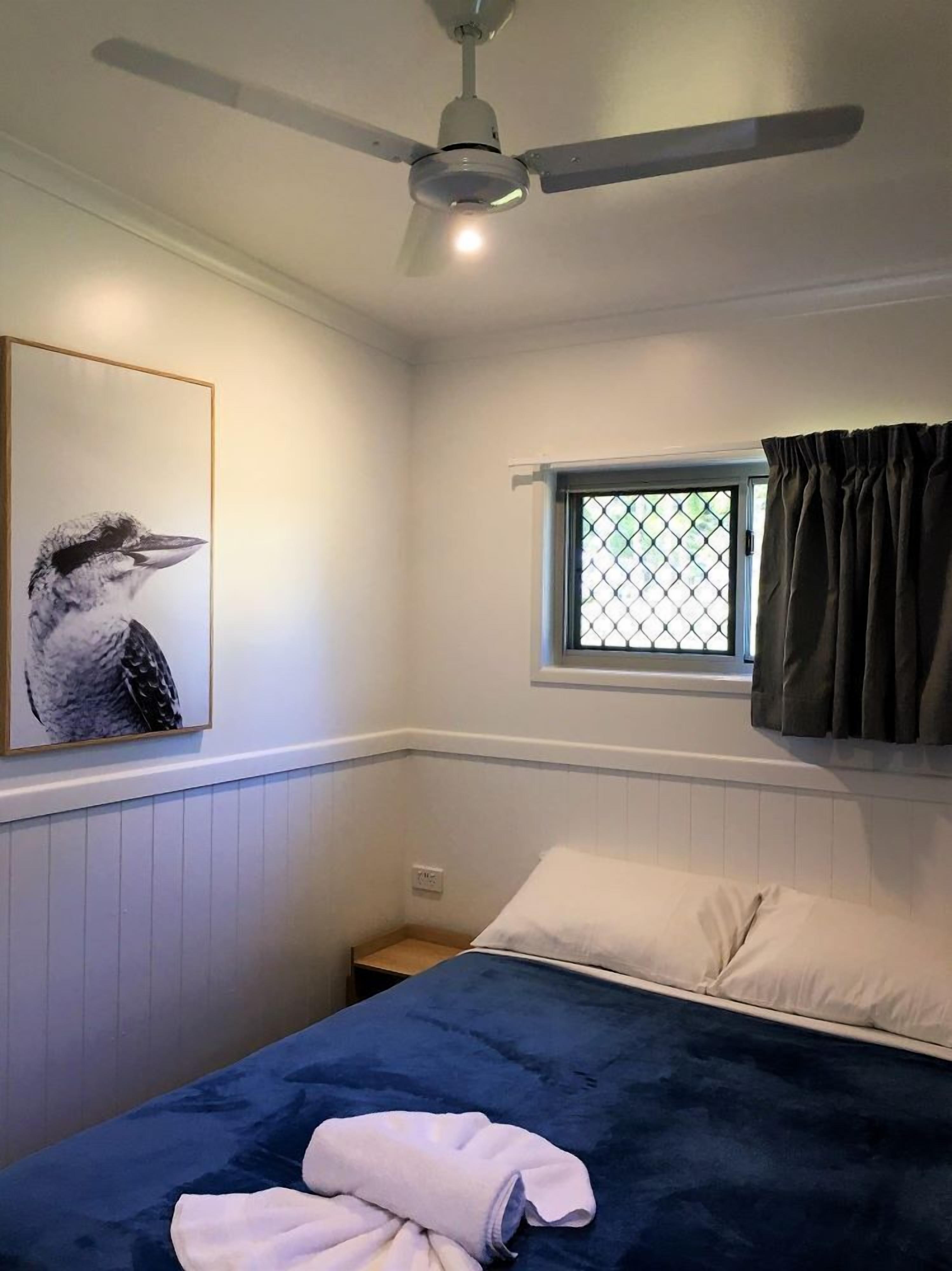 A bedroom with a bed, a ceiling fan, a window with curtains, and a wall-mounted picture.