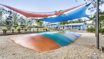 Ein Strand mit einer farbenfrohen Sandinstallation, einem blauen Gebäude und einem eingezäunten Bereich mit Bäumen.